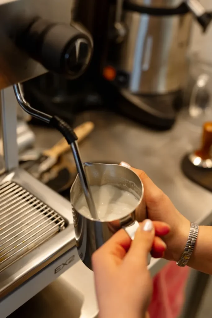 Barista puto pieną kavai metaliniame ąsotėlyje
